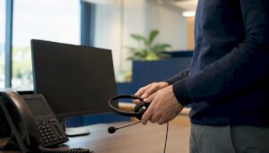 Primer plano de unas manos sujetando un auricular en una moderna sala de atención telefónica
